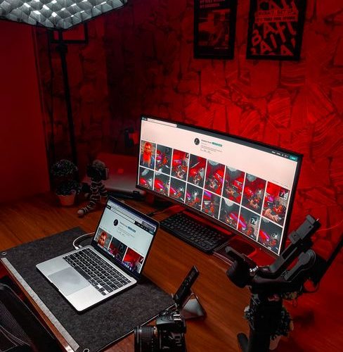 Stylish video editing setup featuring laptop and ultrawide monitor with striking red lighting.